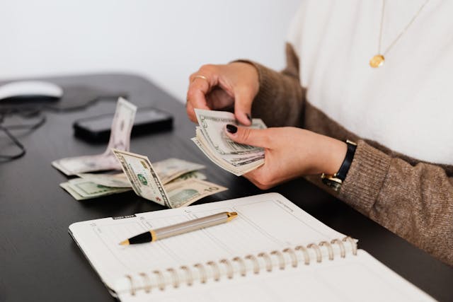 Person counting money overtop of a notebook and pen