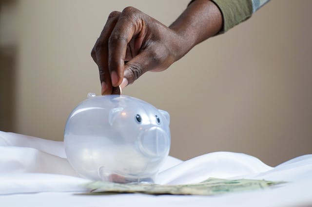 person putting a coin in a clear piggy bank