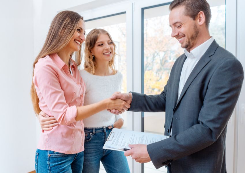 Two smiling tenants shake the hand of a property manager in a suit.