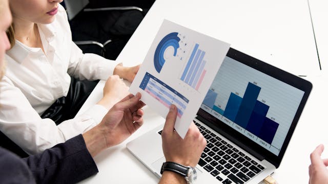 Man and woman looking at charts on laptop and paper